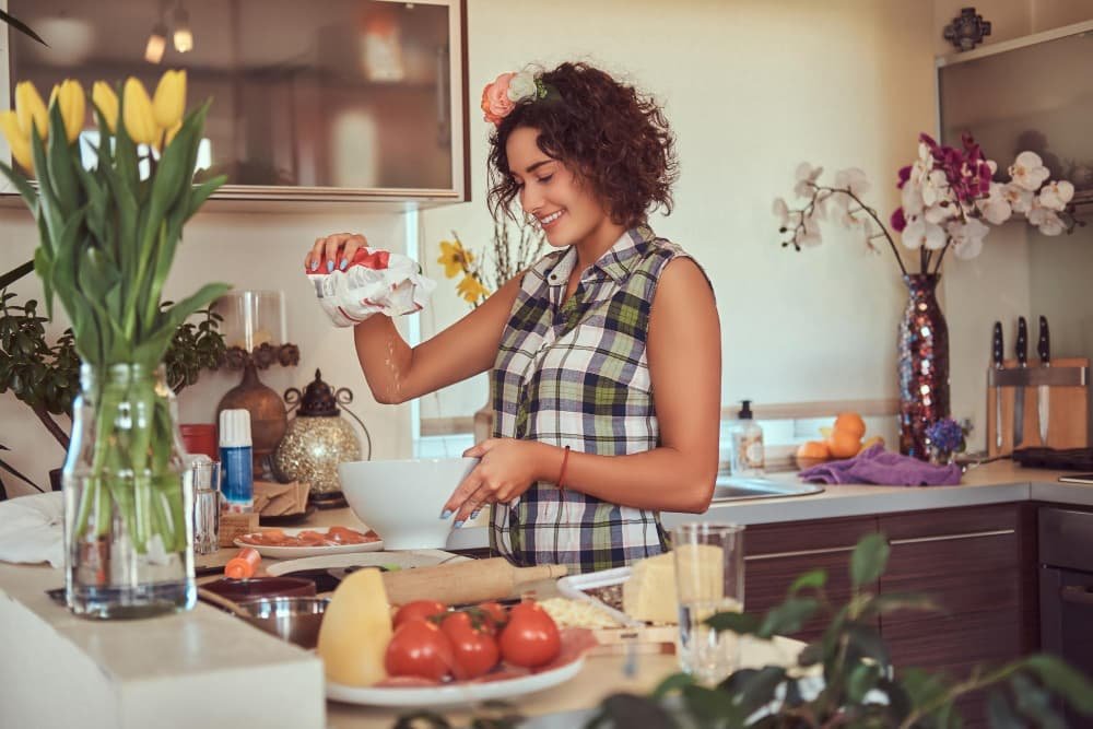 La charmante fille bouclée verse la farine dans une assiette
